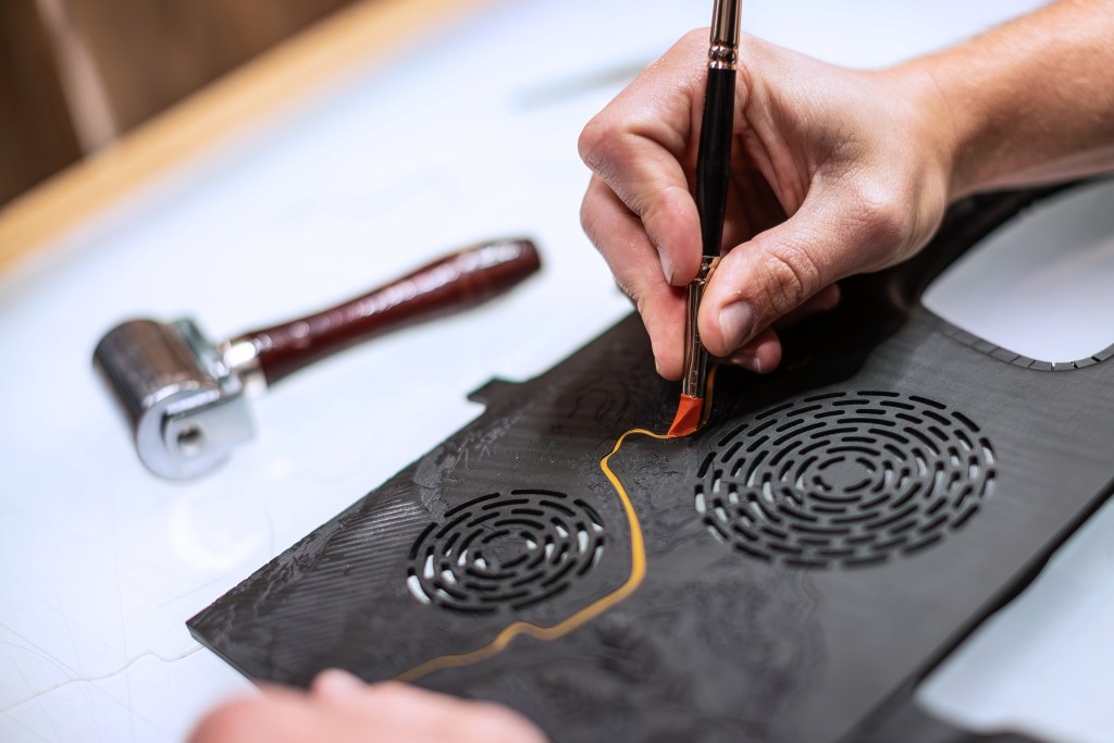 A person is applying gold details on a wood panel