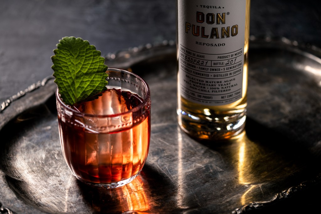 A tequila cocktail in a rocks glass with a green garnish and a bottle of Don Fulano Reposado on the right side of it.