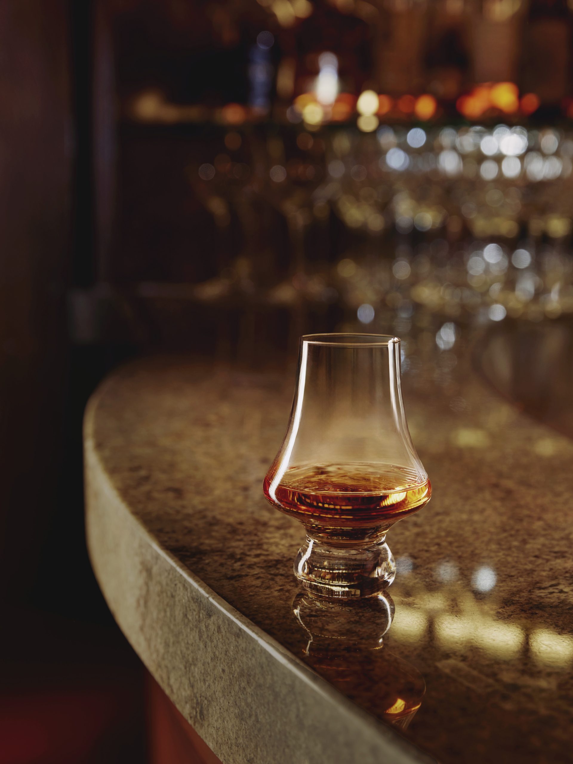 A snifter of whisky atop a gold round table.