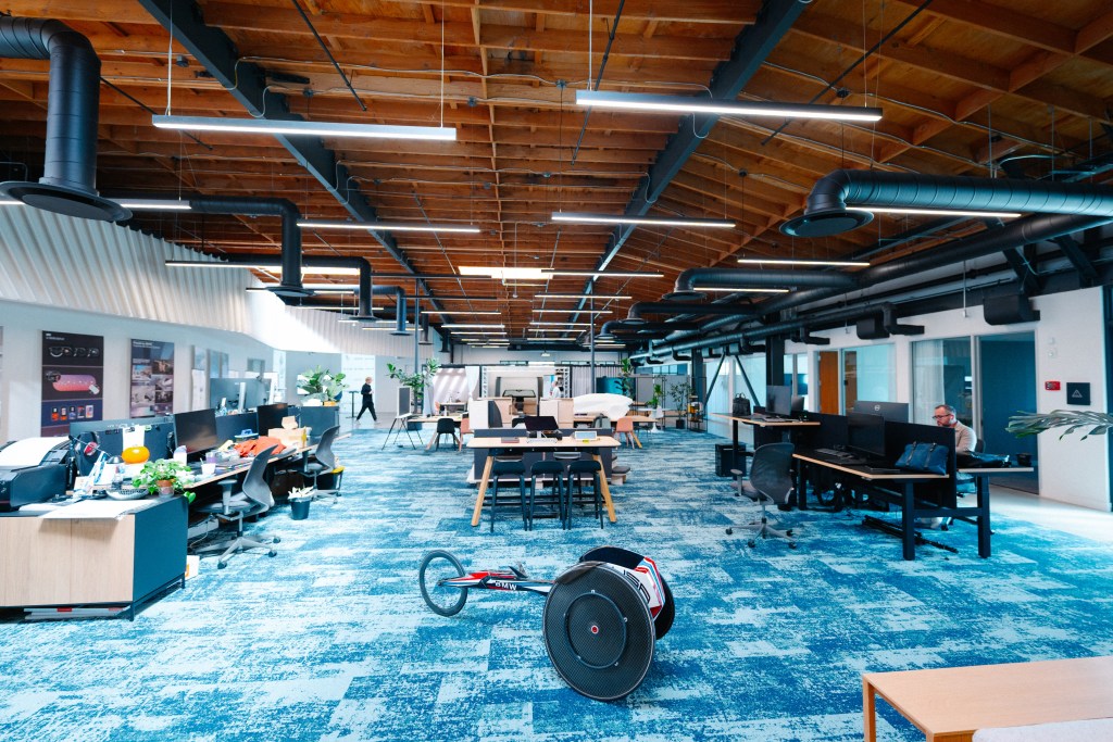 A wood-ceilinged room with blue carpet and desks.