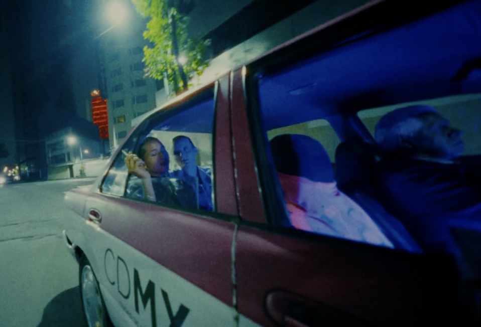 A taxi at night that says CDMX on the side with two people riding in the back seat.
