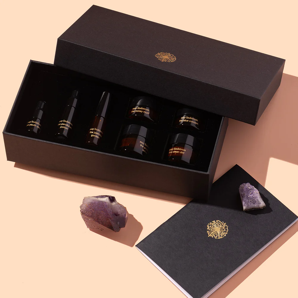 An open gift box of Mae Lindstrom Skin's The Chocolate Box sampler set, shown on a plain background with some crystals