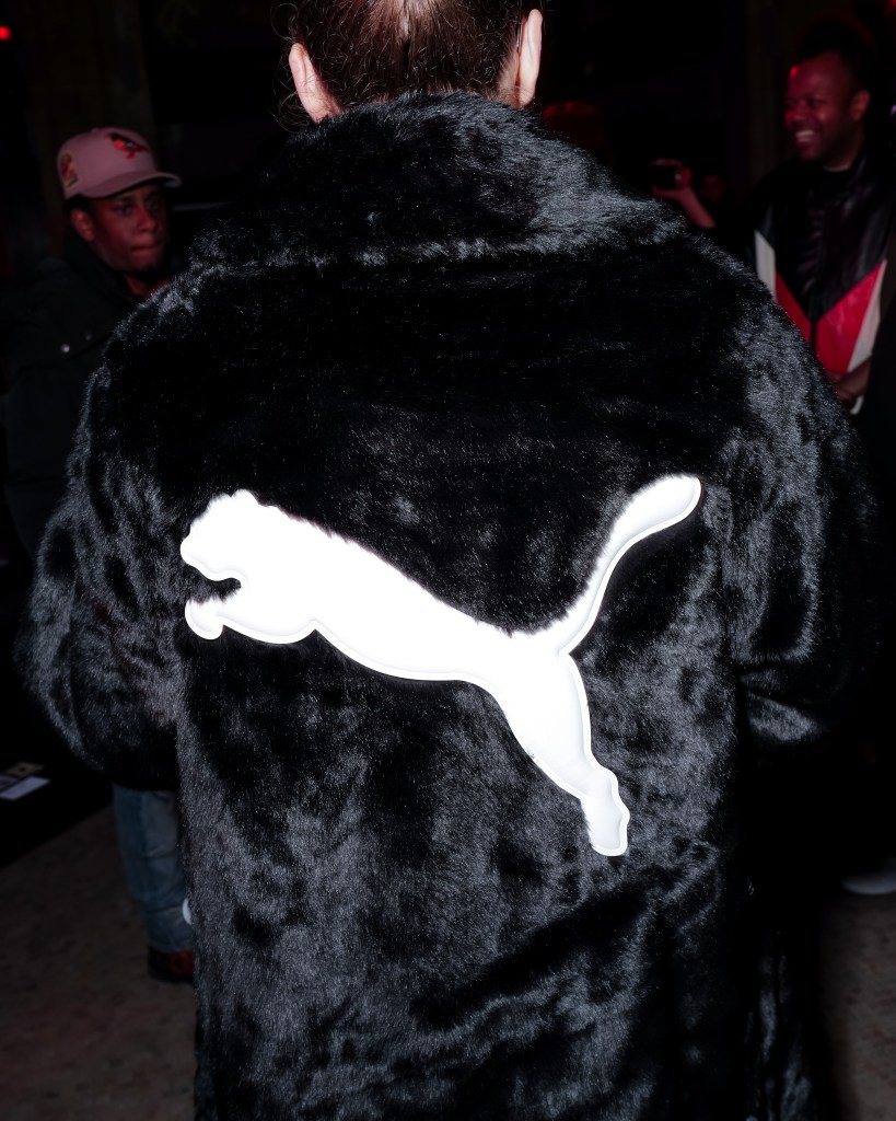 The back of a woman's black fur coat with a white PUMA logo on it.