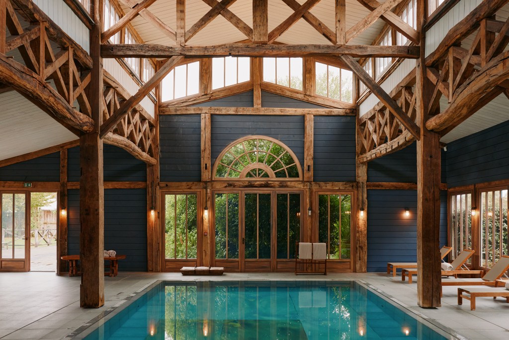 A wood beamed atrium with a blue swimming pool in the center.