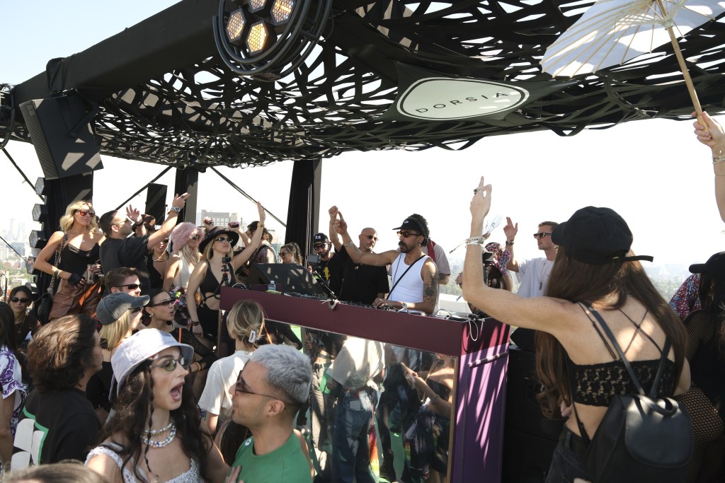 A crowd of people dancing to a DJ on a rooftop in Mexico City with a white Dorsia sign hanging above the DJ booth.