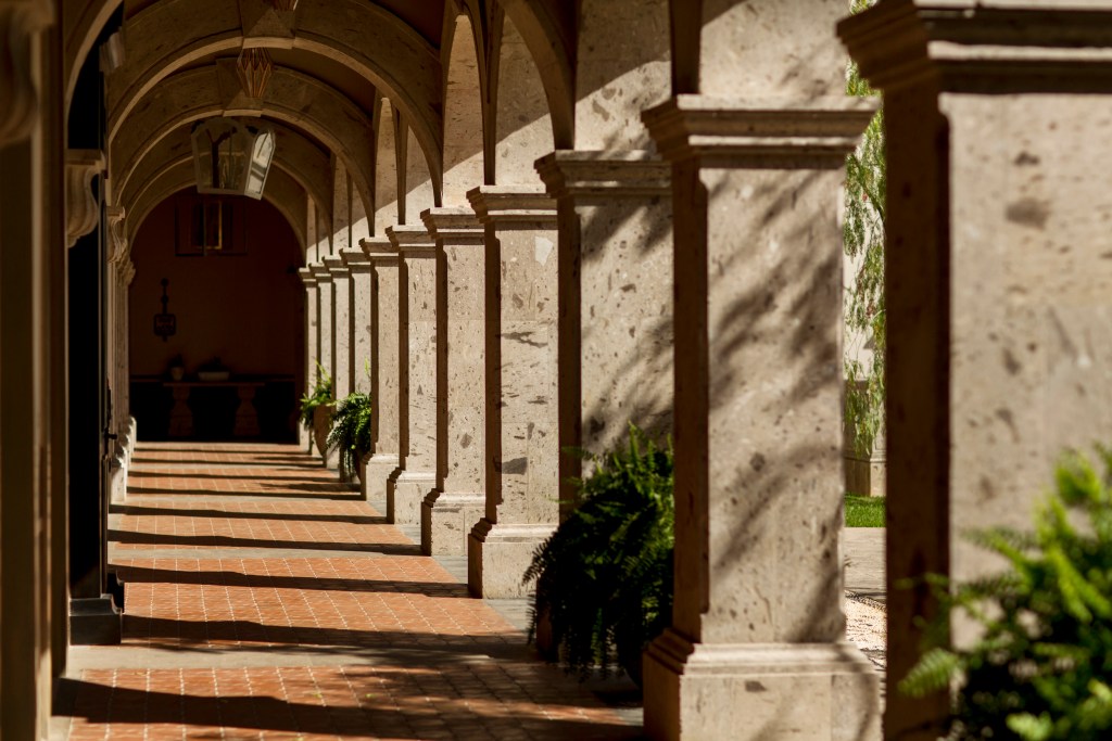 An outdoor hallway with large stone columns and archways.