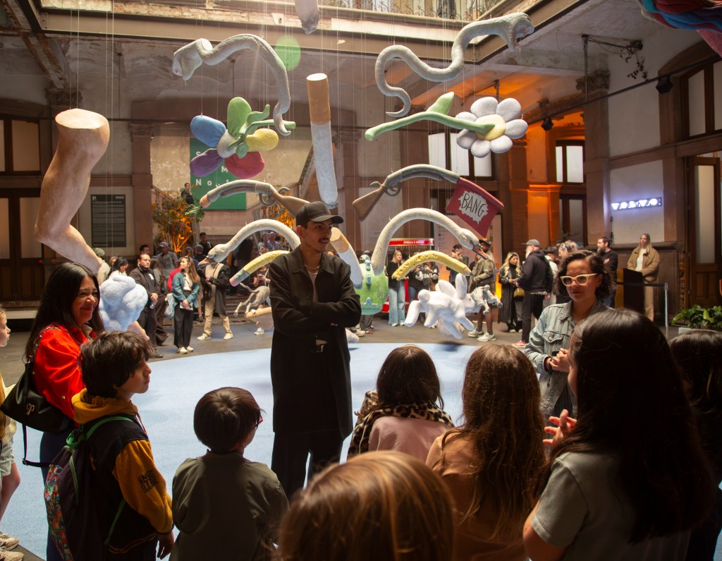 Enrique López Llamas stands in front of his floating clown installation while speaking to a group of children.