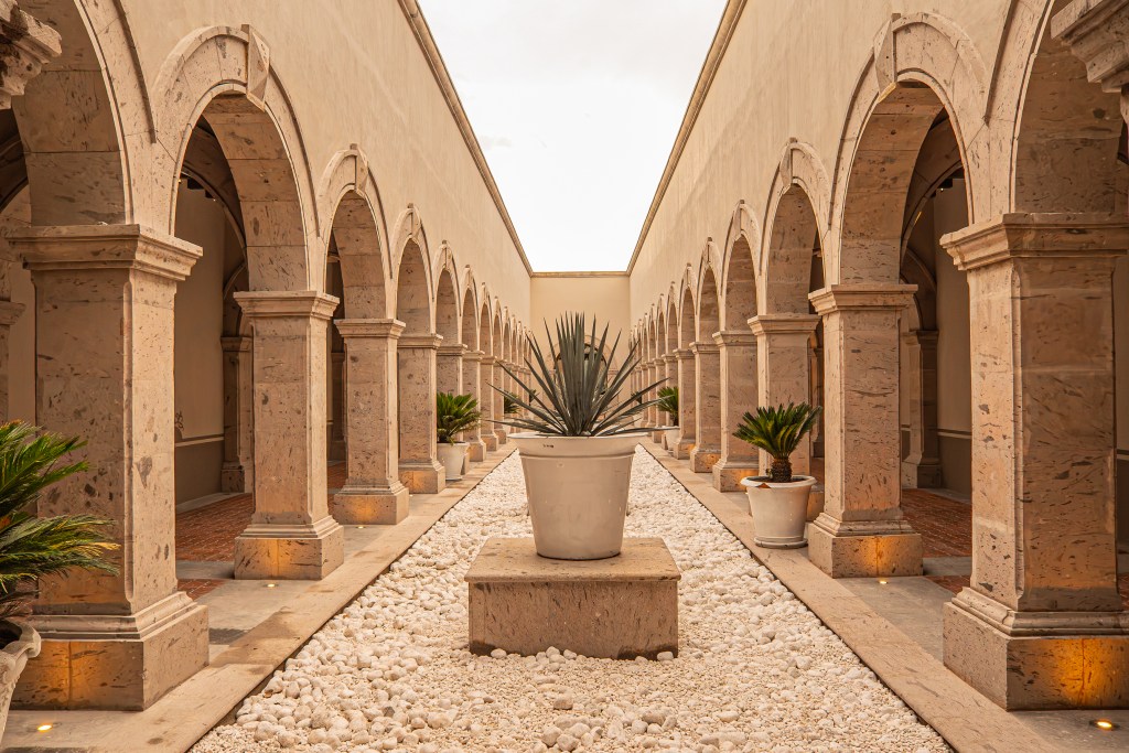 A view into a small courtyard at La Cason with stone arches on both sides and a large potted agave plant in the center.