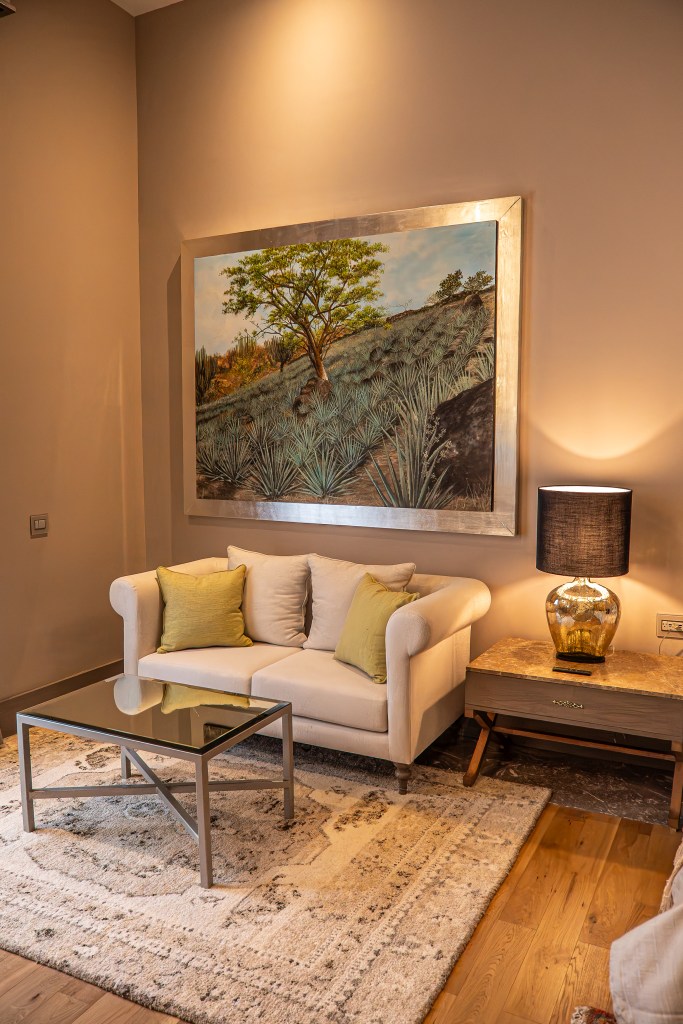 A guest room at La Casona with a white loveseat, a glass tabled and a large framed agave field painting.