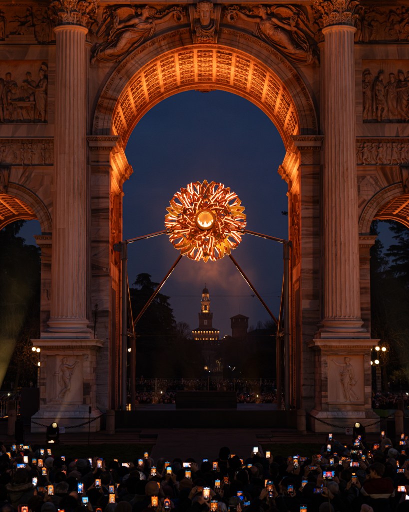 The Cauldron, an orange orb installed under the lit up Arco della Pace. 