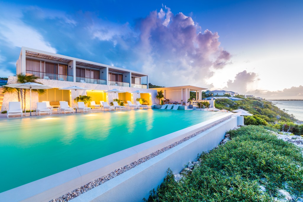 An infinity pool shot at dusk with limestone walls, yellow-lit cabanas and a dramatic cloud in the sky.