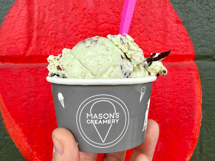 A male hand holding a cup of Mason's Creamery ice cream against a red painted background.