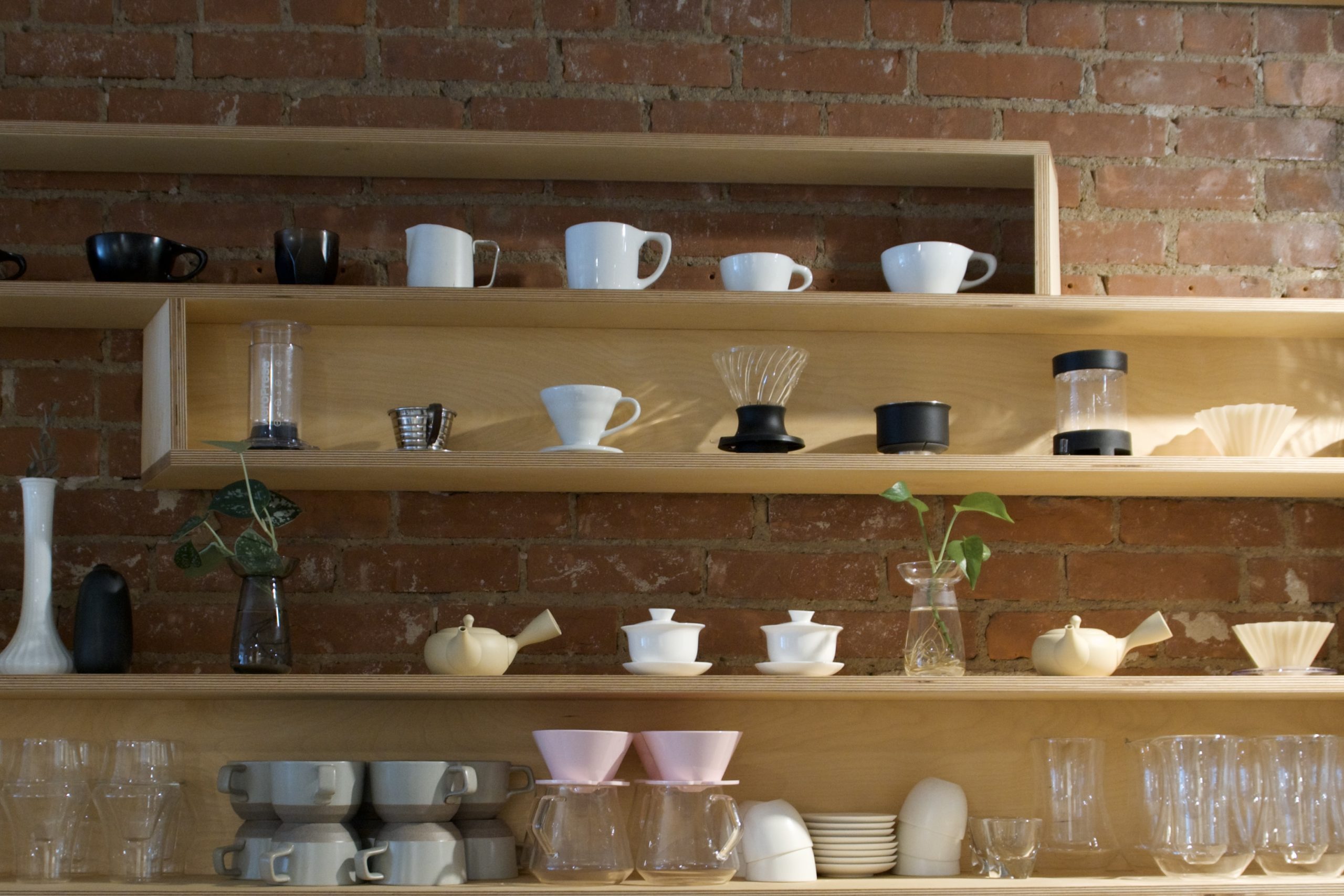A light wood shelf with various coffee mugs and tools.
