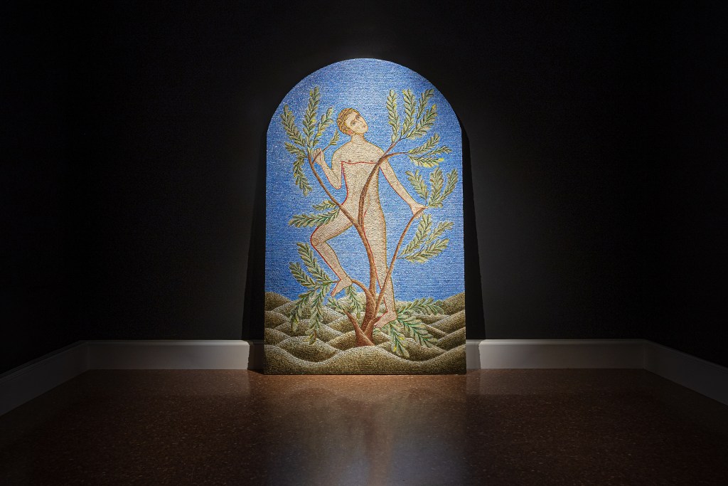 A tall arched mosaic of a nude male figure in a black gallery room.