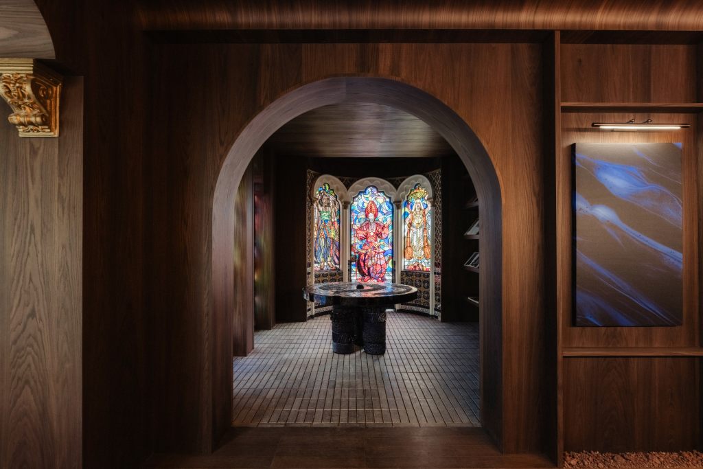 An arched wooden doorway leads to a room with stained glass windows and a central stone table.
