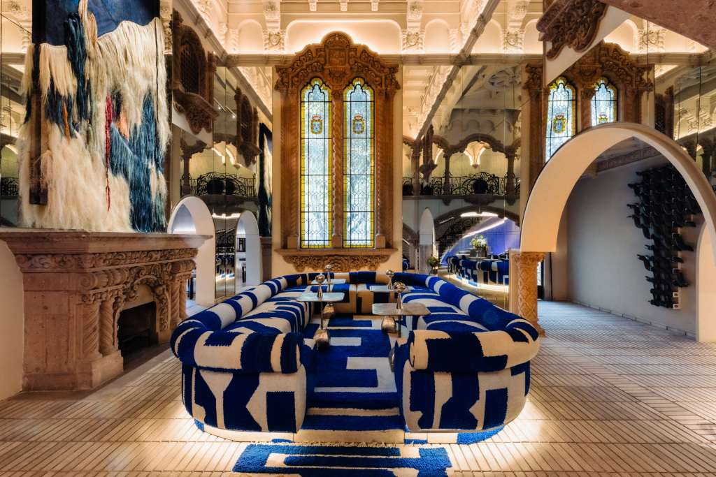 A lounge room with a large blue and white sofa in front of a fireplace with a large woven textile hanging above the mantel.