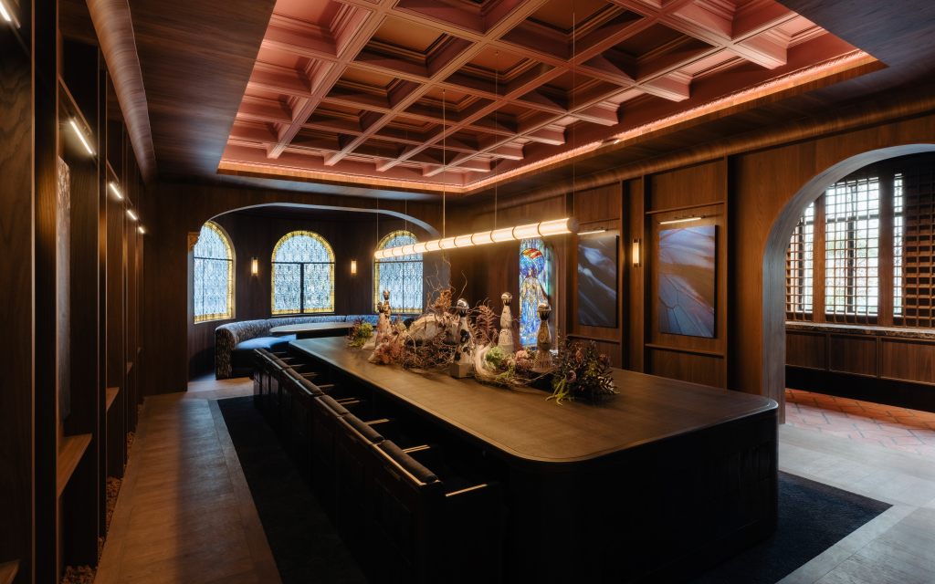A wood-paneled grand room at Casa de los Leones with a large central wooden table, a range of Clase Azul México tequila bottles, a salmon pink tray ceiling and a row of armchairs at the table.