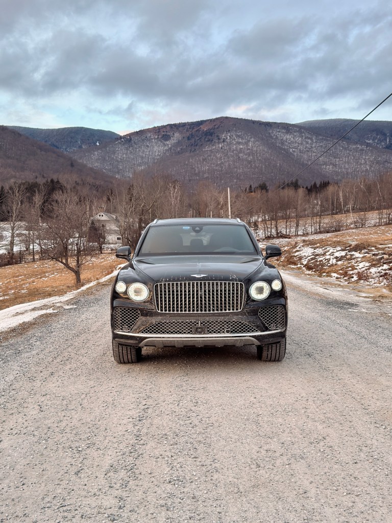 A front view of the 2025 Bentley Bentayga EWB Azure on a gravel road with a low mountain in the background.