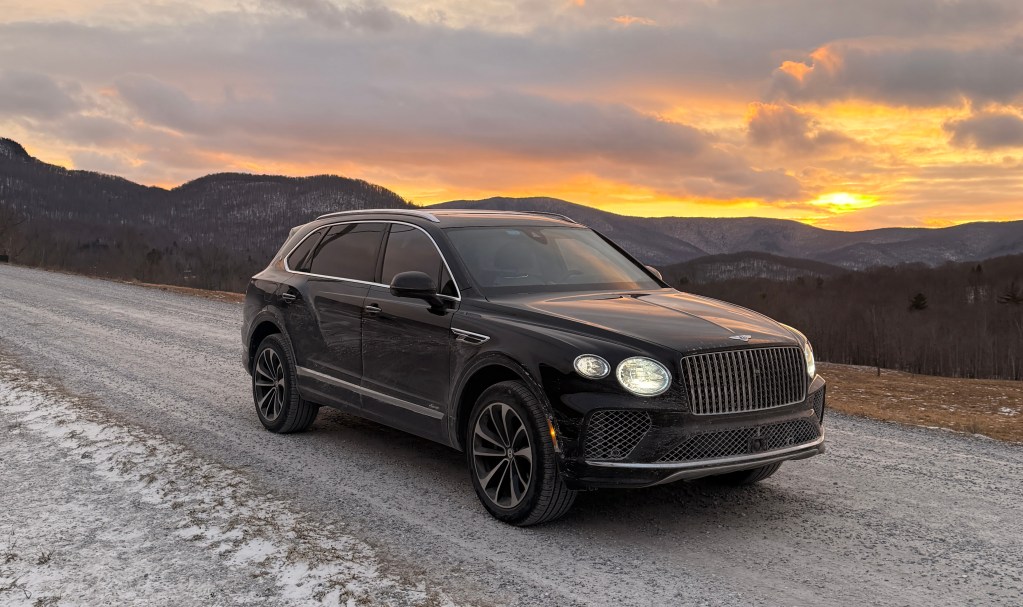 The 2025 Bentley Bentayga EWB Azure shot from a front angle on a gravel road with an orange sunset in the background.