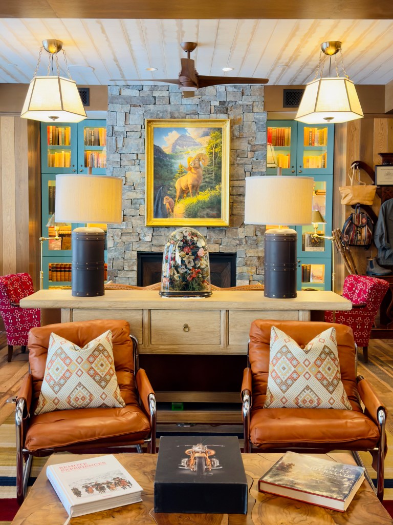The welcome area at the Inn at Sundance Mountain Resort with a stone fireplace flanked by colorful bookshelves, colorful side chairs and a sculptural bell jar installing sitting on a sideboard.