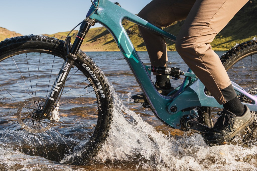 A closeup action shot of a Lauf eElja bike being ridden through shallow water, with water splashing on the tires and legs of its rider.