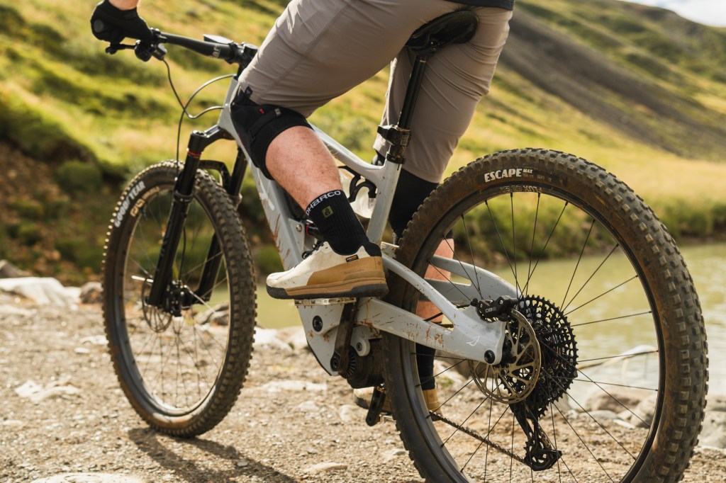 A closeup view of the Lauf eElja bike showing the rear tire while a man rides it on a trail.