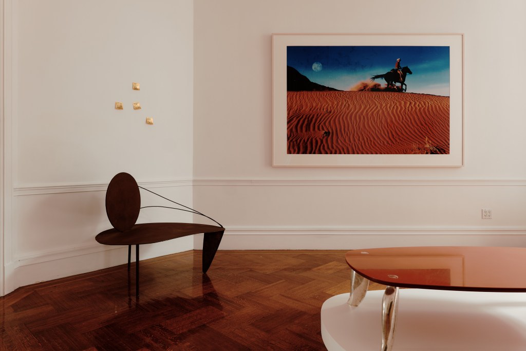 Objects in the image include bronze Post-It Notes by Sebastian Errazuiz and a table by Brett Robinson, a photography of a man on a horse and a chair