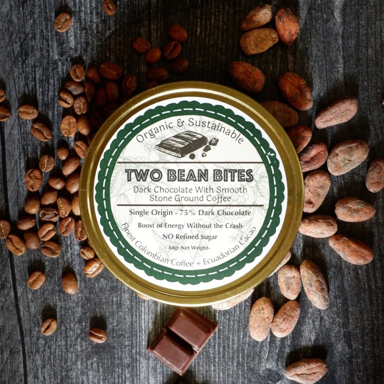 A package of Third Bean's Two Bean Bits coffee infused chocolate on a wood background with coffee beans, chocolate beans and the two bean bites chocolate pieces