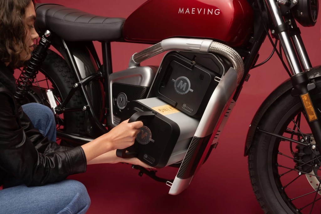 A woman's hand pulling out one of two portable Maeving battery packs out of the Maeving RM2 electric motorcycle.