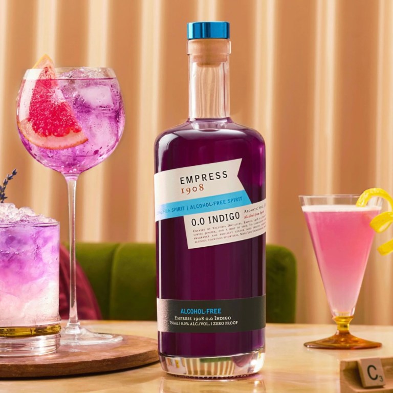 A bottle of Empress 1908 0.0 Indigo gin sits on a table with several colorful cocktails