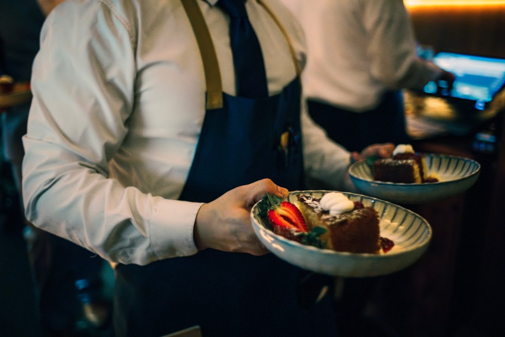 A waiter holds two bowls with servings of cake