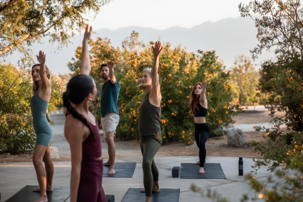 A small group of people taking a yoga class in the gardens of We Care Spa.