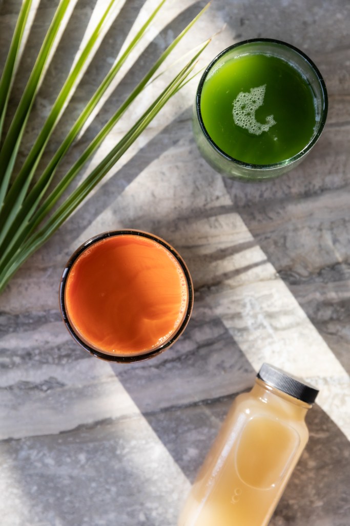 An overhead shot of three kinds of juice and a palm front in the corner of the frame.