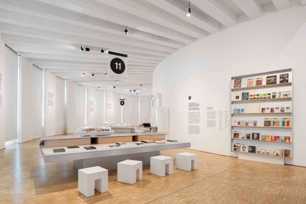 A view of a curved room showing graphic design works by Lella and Massimo Vignelli.