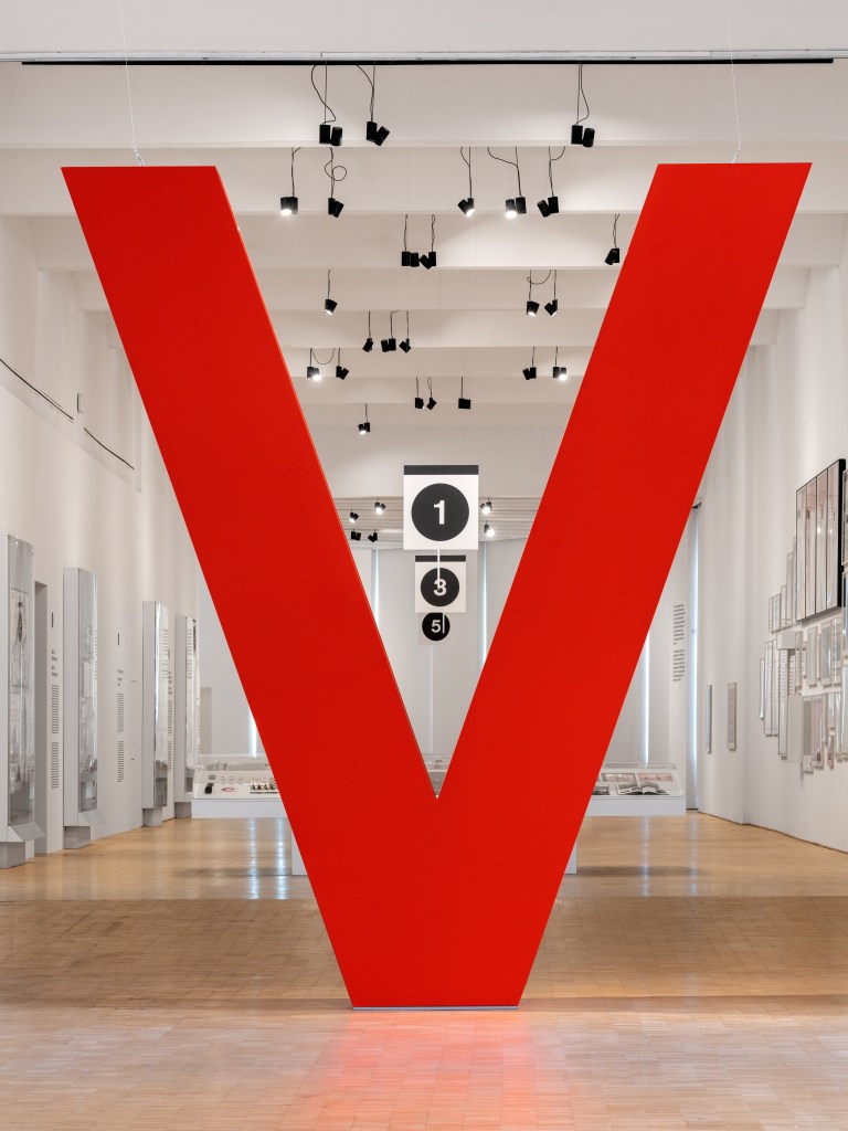 A large red, three-dimensional "V" at the entry to the Vignella exhibit at Triennale Milano.