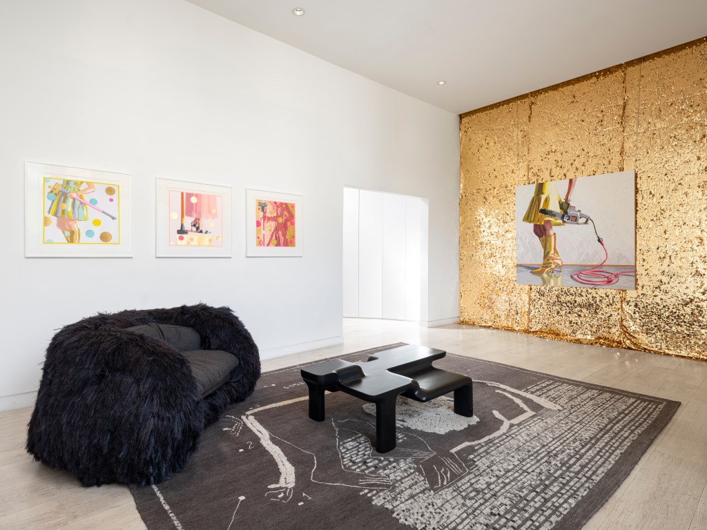 An installation view of Kelly Reemsten's "Fool's Gold" show at Albertz Benda Gallery, with a shiny textured gold wall, gold dress paintings and black sculptural furniture.