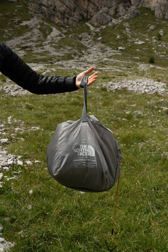 A male hang holding the Universal One Bag's stuff sack in front of a grassy and rocky background.