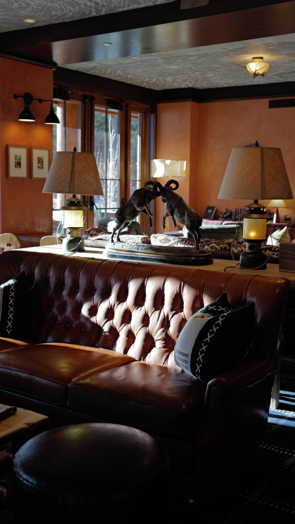 A lounge room at the Inn at Sundance Mountain Resort with a tufted leather sofa, an electric lantern, heavy metal animal sculptures and sunny windows.