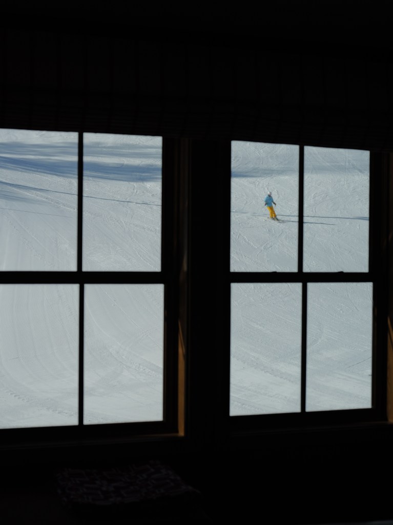 An image of a person skiing outside wearing a blue and yellow ski outfit, shot from inside looking out a window.