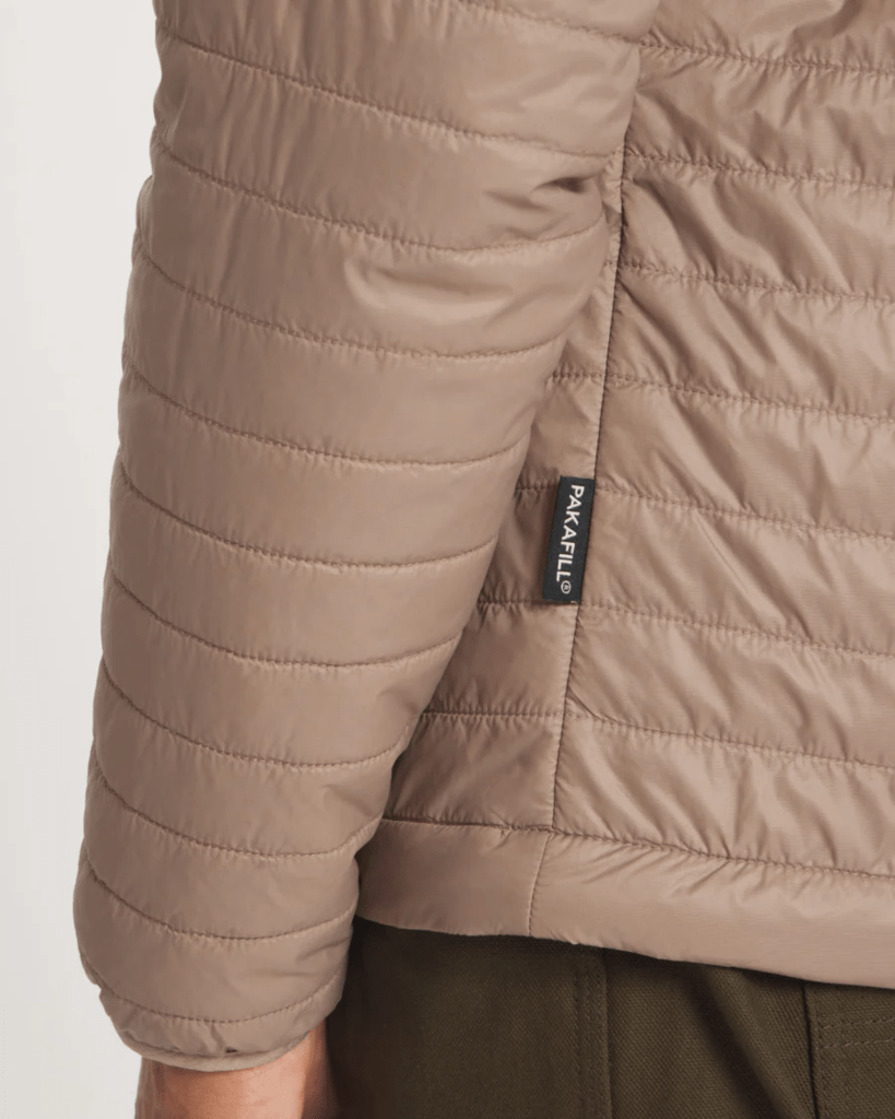 A detail of a man's arm wearing an insulated jacket with a black PAKAFILL tag sewn into the side seam.