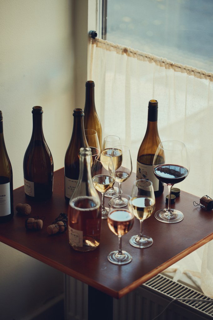A small wooden table with several bottles of Oddbird non-alcoholic wine and partially filled wine glasses.