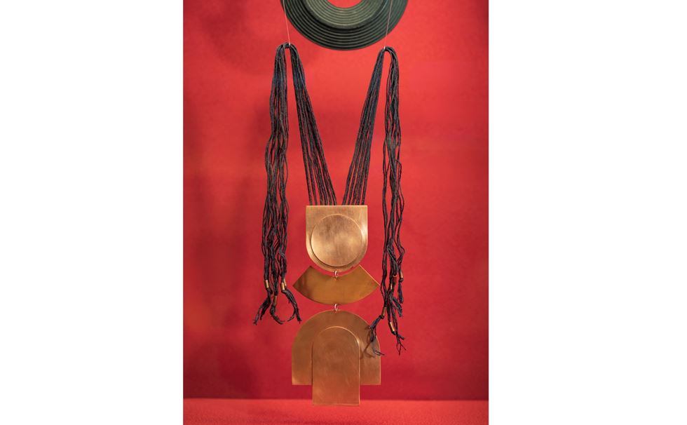 A red background with a brass and hair sculpture by Simone Brewster.