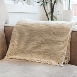 Rest & Reset's cotton Ceremony throw blanket is draped over the arm of a sofa