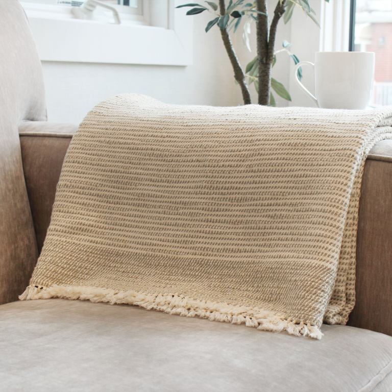 Rest & Reset's cotton Ceremony throw blanket is draped over the arm of a sofa