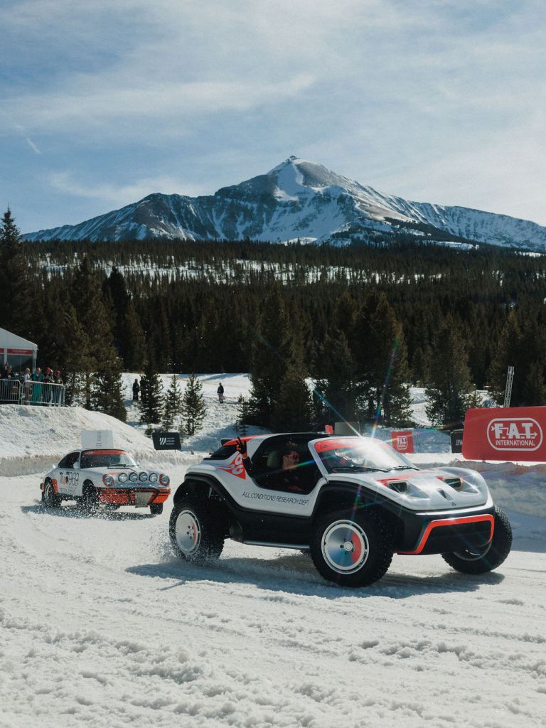 Two cars driving on a curve on a snowy track with a mountain in the background.