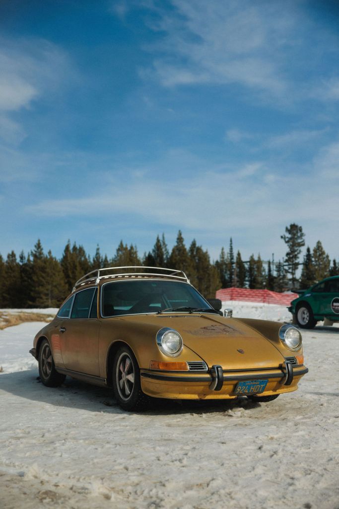 A gold race car on a snowy track with evergreen trees in the background.