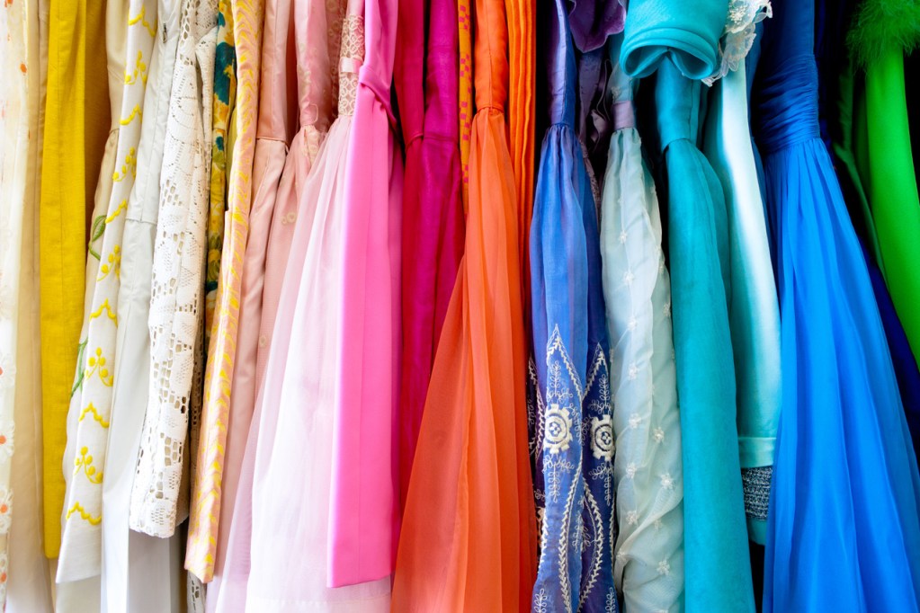 A cropped shot of a row of colorful vintage dresses hanging from a rack.