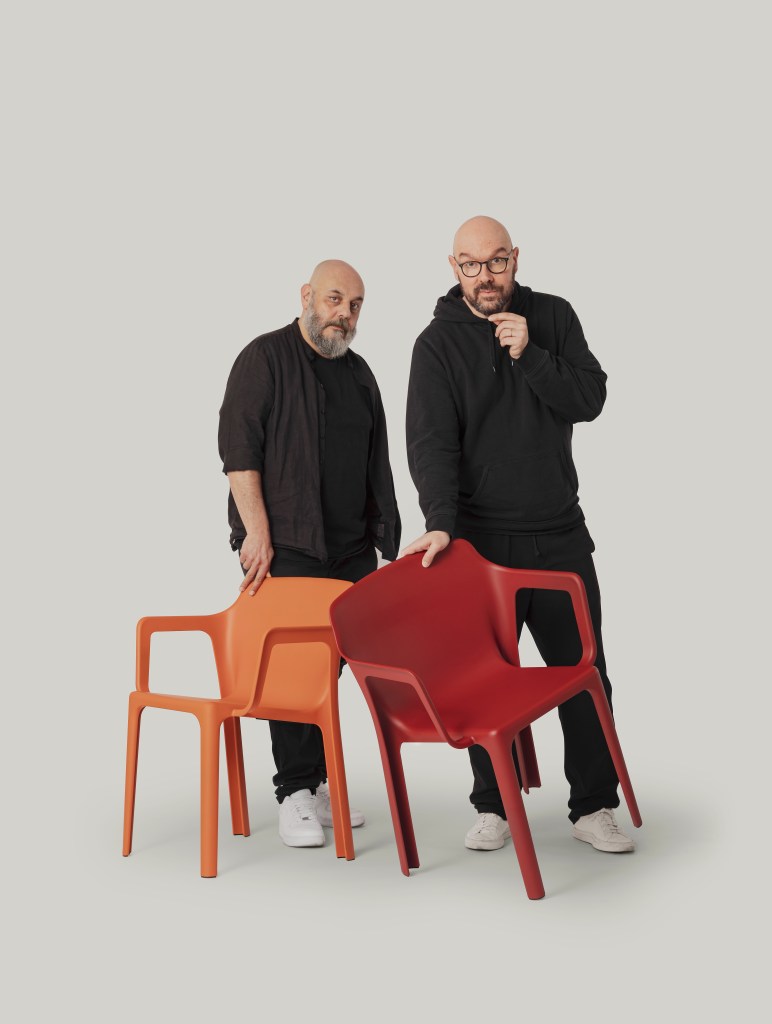Two designers wearing all black, standing next to each other while touching two Linnea chairs.