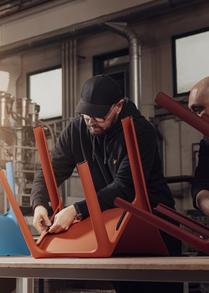A man in a factory putting finishing touches on the underside of an orange Linnea chair.