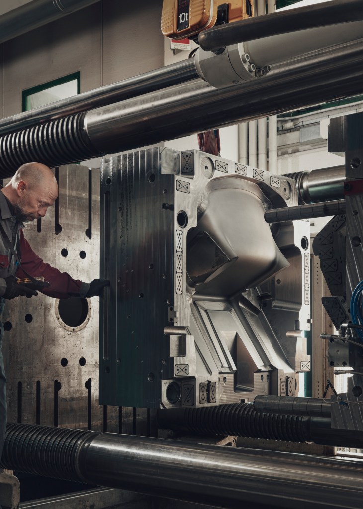 A man in a factory adjusting a machine with a Linnea chair mold.